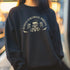 Christmas sweatshirt with "SEASONS SCREAMINGS, DARKLING" text arched over a skull wearing Santa hat. Bats, flowers, and ornate designs surround the skull in vintage-inspired style.